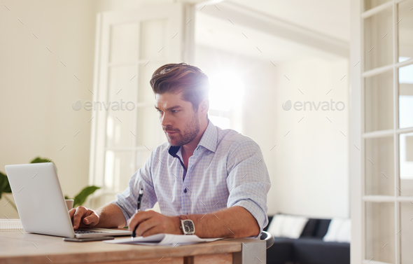 Young man working on laptop and writing notes