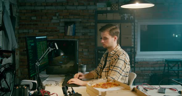 Coder Man or Hacker Eats Pizza Working on Computer in Loft Electronics Workshop