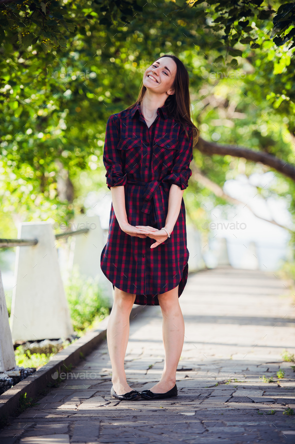 Beautiful, pretty woman in casual checkered dress walking at park outdoors. Street fashion style.