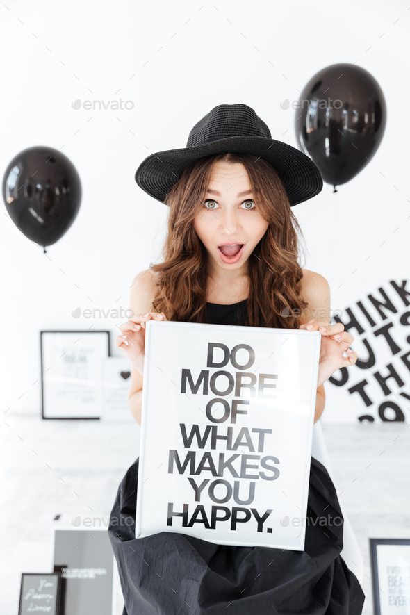 Surprised funny woman holding white board over black balloons background