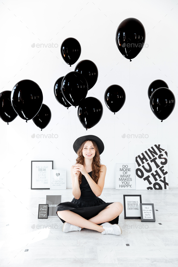 Happy woman sitting with legs crossed and holding black balloons