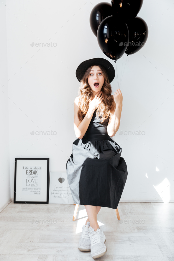 Surprised lovely young woman holding black balloons