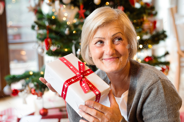 Beautiful senior woman in front of Christmas tree with present