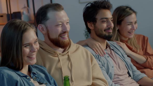 Two Couples Watching TV Laughing and Drinking Beer in Apartment at Night alt