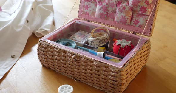 Close up on the hands of an old woman seamstress and her sewing kit as she prepares a white dress sh alt
