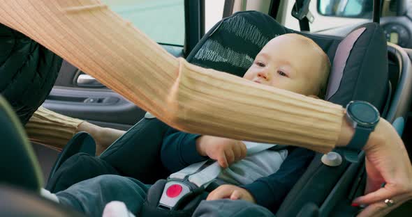 Closeup Baby Boy Who Sits in the Baby Car Seat Inside of Car Door Opens and His Mother's Hands alt