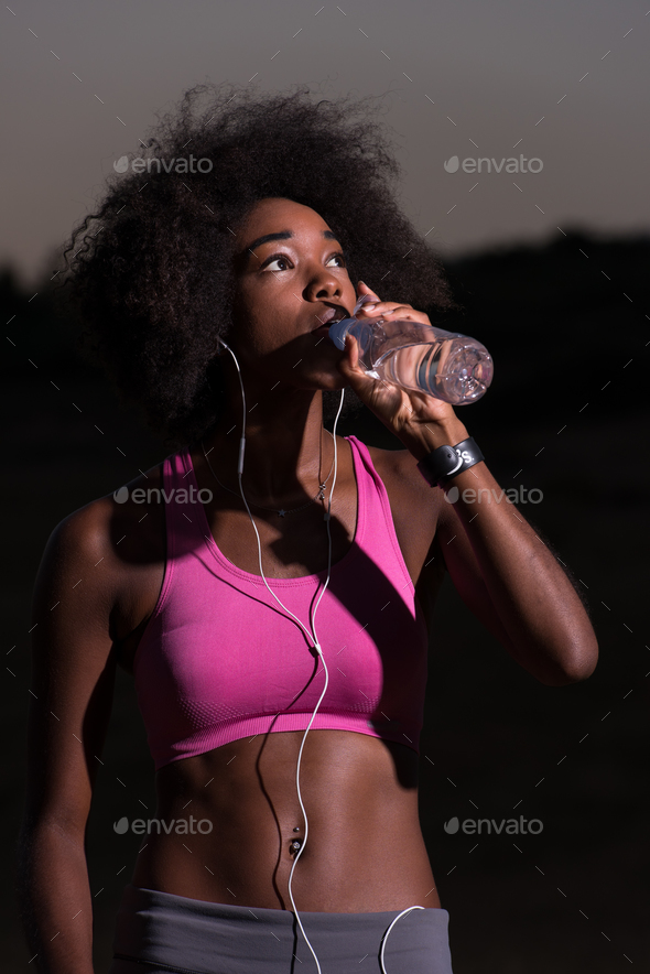 african american woman drinking water after jogging in nature