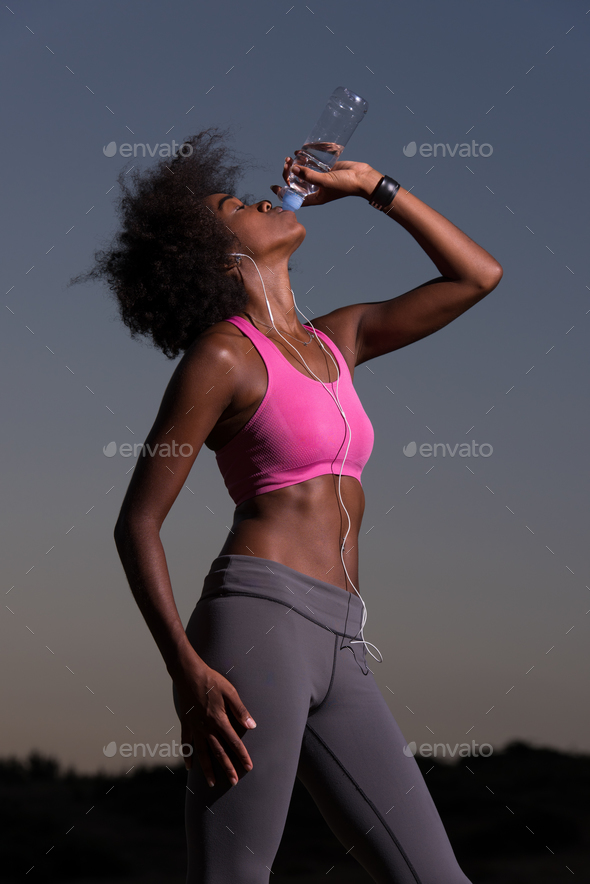 african american woman drinking water after jogging in nature Stock Photo by dotshock