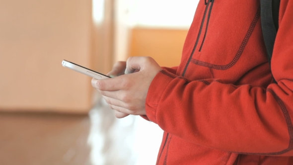 The Teenager Holding a White Mobile Phone Indoors alt