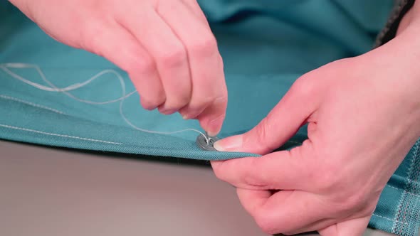 Close-up of woman hands sewing a button. The dressmaker sews a button on a clothes. alt
