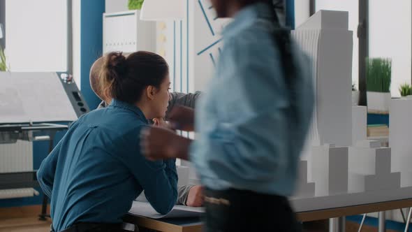 Colleagues Doing Teamwork to Design Construction Layout with Building Model and Blueprints alt