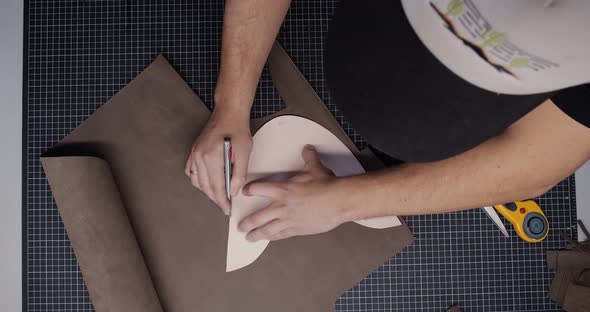 Top View of Tailor with Knife Passing Around Pattern on Leather Piece Preparing Blanks for Making