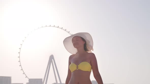Girl in the Yellow Swimsuit and a White Hat Puts Hands Up and Enjoying Vacation
