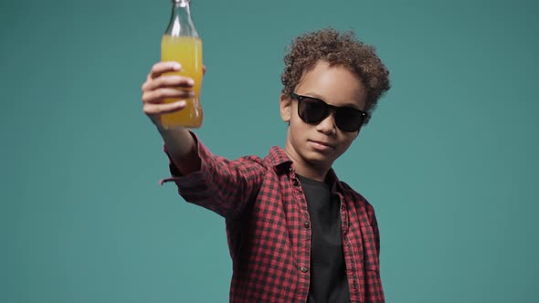 Boy Wearing Big Black Sunglasses and Showing Juice in Bottle to the Camera