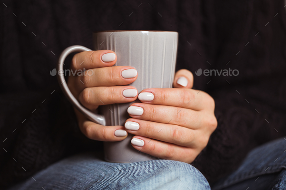 Woman with beautiful manicure holding a gray cup of tea - Stock Photo - Images