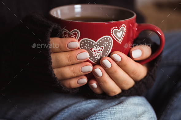 Woman with beautiful manicure holding a red cup of tea - Stock Photo - Images