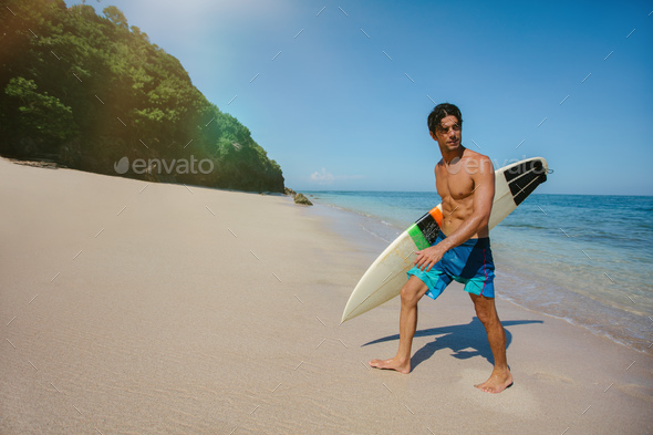 Male surfer holding surf board walking out of the sea - Stock Photo - Images