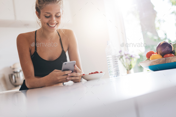 Smiling woman using smartphone in kitchen - Stock Photo - Images