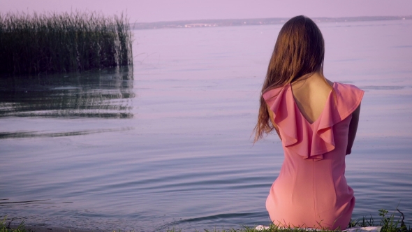 Lonely Woman in a Pink Dress Sitting on the Bank of the Pond.