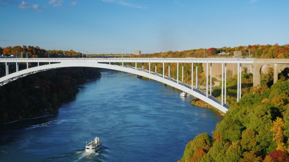 Small White Ship Sails Under the Bridge Over the River Niagara alt