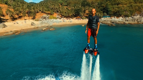 Aerial: Man Standing Over the Water on Flyboard Near the Beach  alt