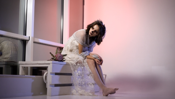 Young Girl in White Dress and Veil Participating in Halloween Party Sitting in the Room. with alt