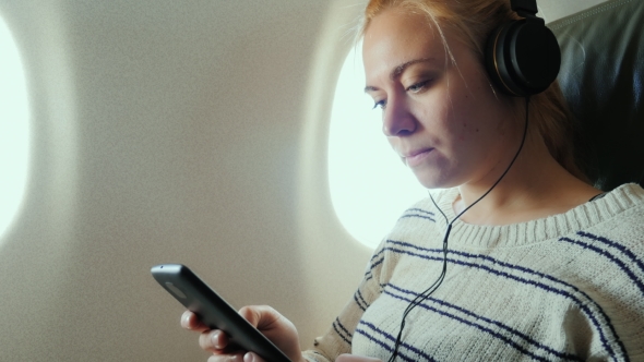 Young Attractive Woman Is Flying in an Airplane. It Uses a Smartphone Listening To Music alt