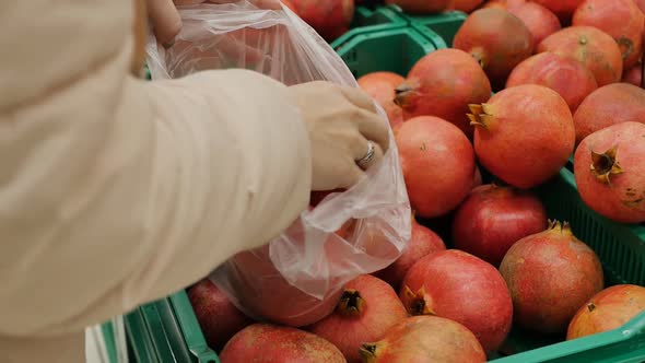 A Woman's Hand Picks a Ripe Red Pomegranate in the Market and Puts It in a Bag alt