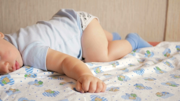 Beautiful Baby Sleeping in Funny Pose on a Bed. Under the Baby Diaper, the Boy About a Year
