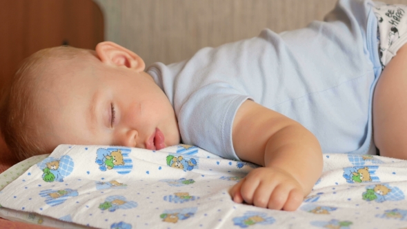 Beautiful Baby Sleeping in Funny Pose on a Bed. Under the Baby Diaper, the Boy About a Year