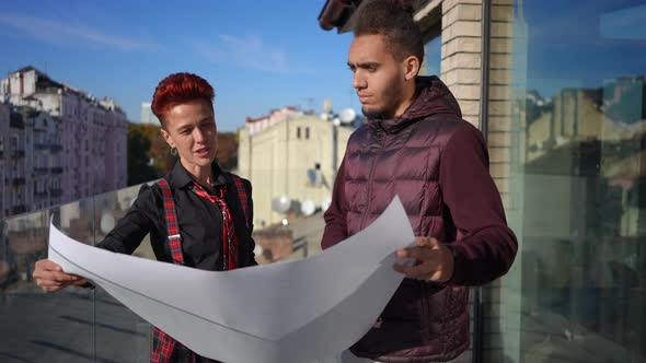 Pierced Caucasian Woman and African American Young Man Talking Analyzing Blueprint Standing on alt