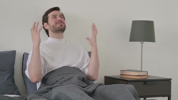 Young Man Feeling Worried While Sitting in Bed alt