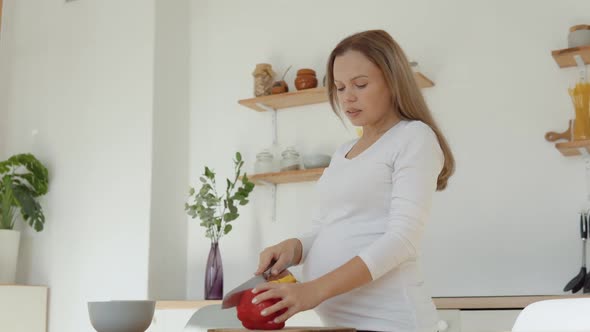 Pregnant Fairskinned Woman in the Kitchen Cuts Red Pepper alt
