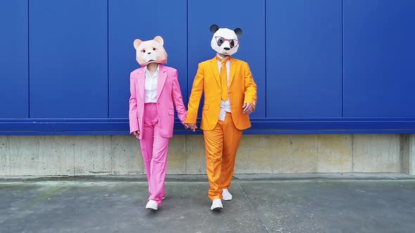 Business couple wearing animal masks holding hands against blue wall