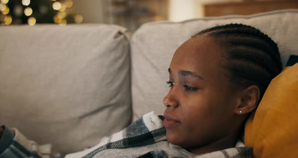 An Upset Africanlooking Girl is Wearing Plaid Shirt Lying on Sofa in the Living Room and Watching alt