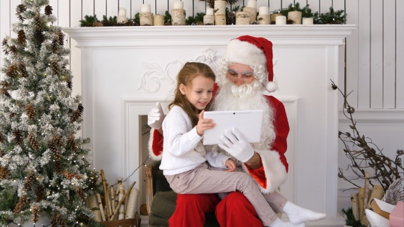 Happy Little Girl Showing Surprised Santa Presents on Tablet alt