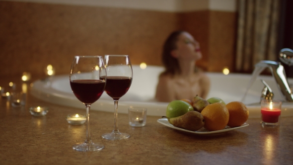 Sexy Young Woman Relaxing in Foam at the Background of Romantic Lunch of Fruits and Wine