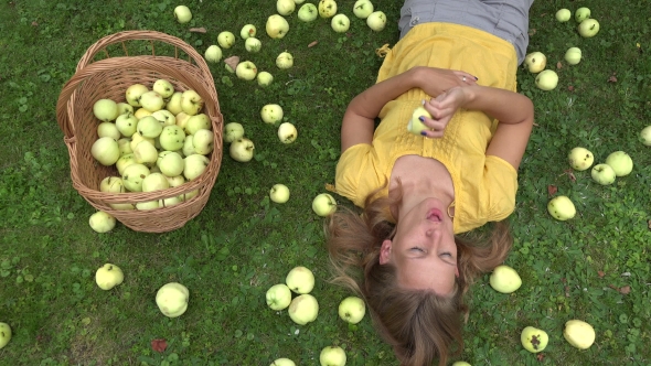 Young Woman Lie on Grass in Orchard and Eat Juicy Apple