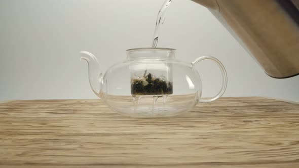 Pouring Boiling Water From Kettle Into White Tea in a Teapot on a Wooden Table alt