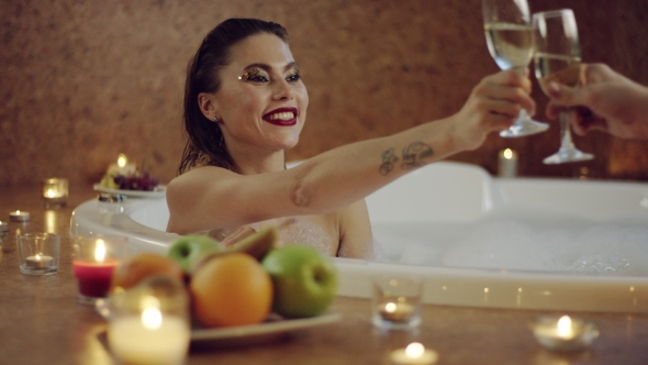 Beautiful Woman Clinking Glasses of Champagne in Bath