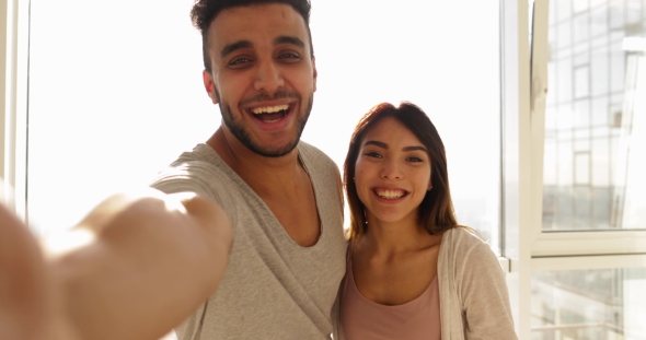 Young Mixed Race Couple Taking Selfie Photo Over Big Window Morning Sunlight, Happy Hispanic Man