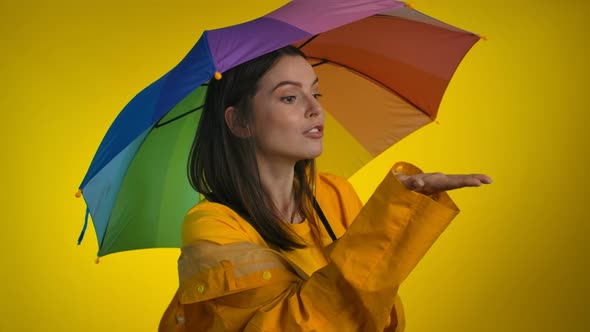A Playful Woman in a Bright Yellow Raincoat with a Rainbow Umbrella alt