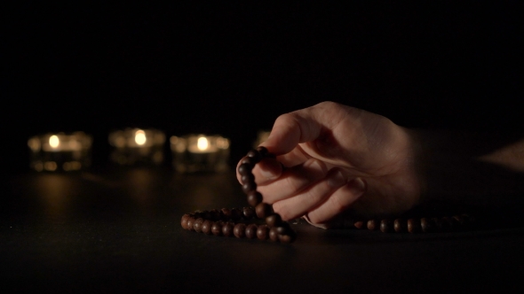 Male Hand Holding Rosary Beads, on Black Background
