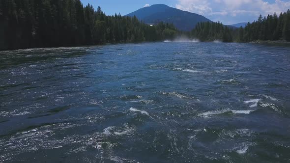 Aerial Drone Traveling Low Along Flowing Water With Mountains In Background 1 alt