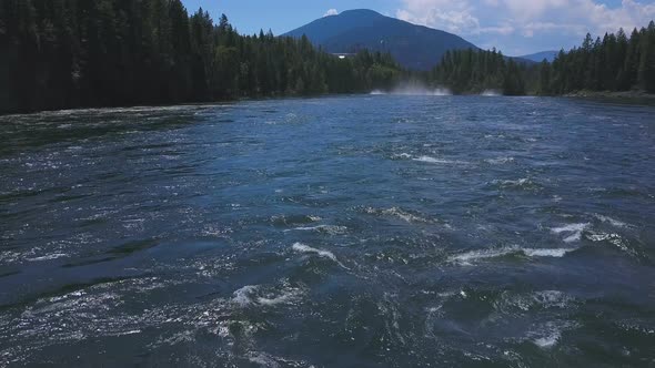 Aerial Drone Traveling Low Along Flowing Water With Mountains In Background 1