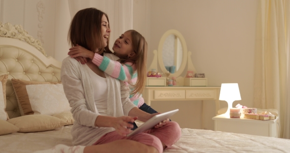 Mother With Daughter Embrace On Bed Using Tablet Computer Happy Smiling Young Family