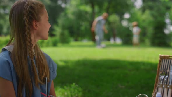 Calm Girl Watching Football Training Father with Son on Green Lawn Closeup alt