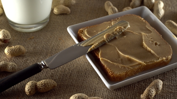 Tasty Peanut Butter Being Spread on White Toast and Milk