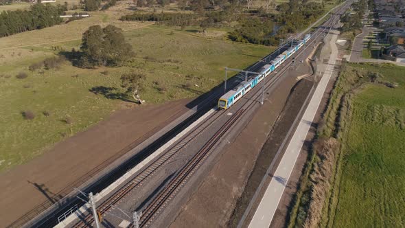 Train drives through outer suburbs aerial shot rising alt