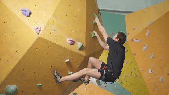 Physically Strong Man Climbing on High Artificial Rock in Sports Club